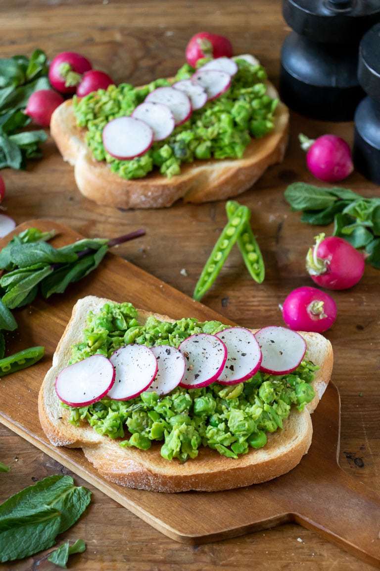 Close up of a slice of toast topped with mashed peas and a row of radish slices.