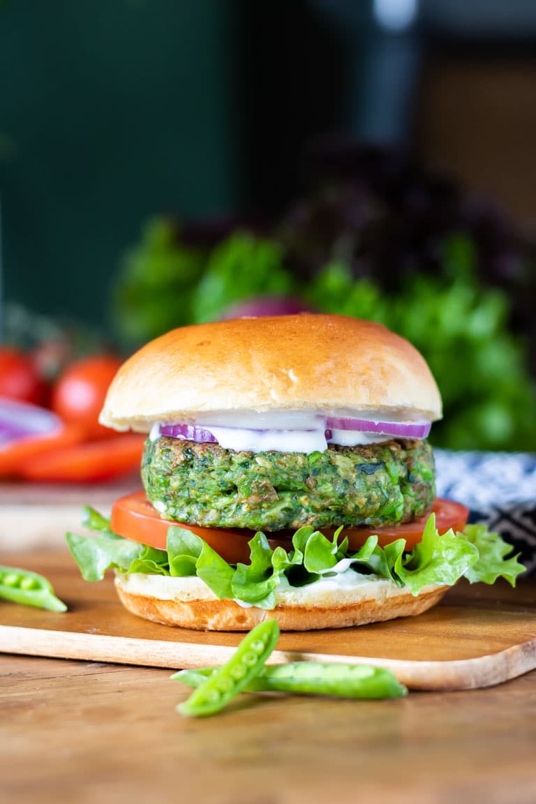 A burger bun with lettuce, tomato, onion, mayo and a bright green vegan burger patty made from spinach and peas.