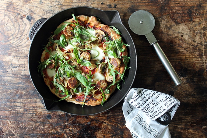 Pizza in a skillet with pizza cutter and tea towel.