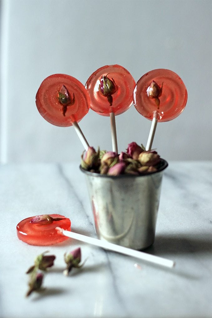 Close up of lollipops sticking out of a metal cup with rose buds.