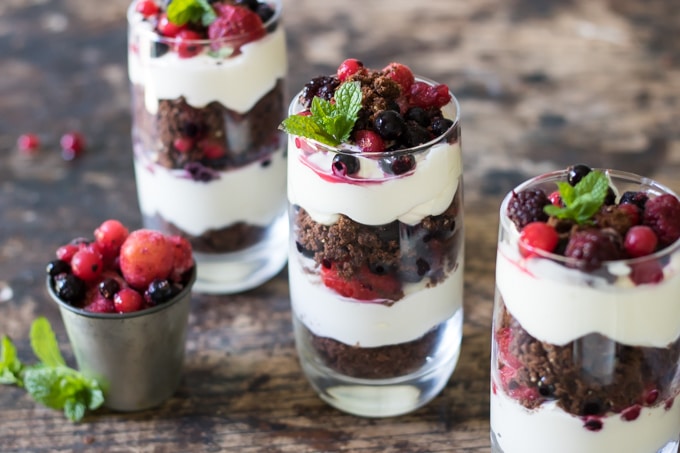Cookie Cheesecake Parfait with Berries in glasses next to a pot of berries. The layered dessert is ready in minutes.