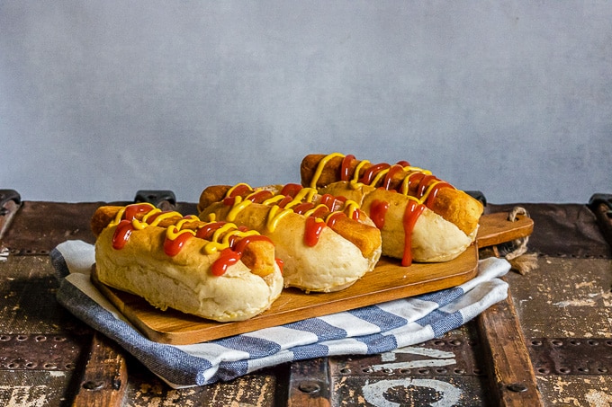 A wooden board with three lentil carrot hot dogs in buns with mustard and ketchup