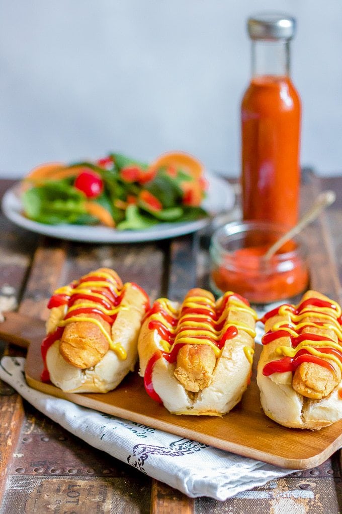 Lentil carrot veggie dogs in buns with ketchup and mustard in front of a bottle of ketchup and a salad