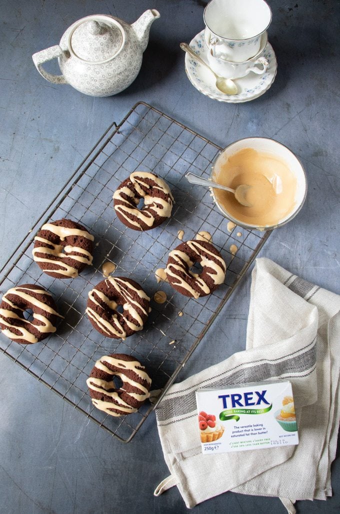 Baked chocolate vegan doughnuts with earl grey glaze on a vintage rack with a bowl of drizzle, teapot and vintage teacups.