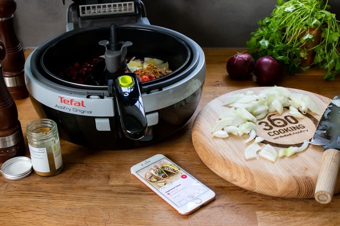 Tefal Actifry Original air fryer, next to a chopping board with onions.