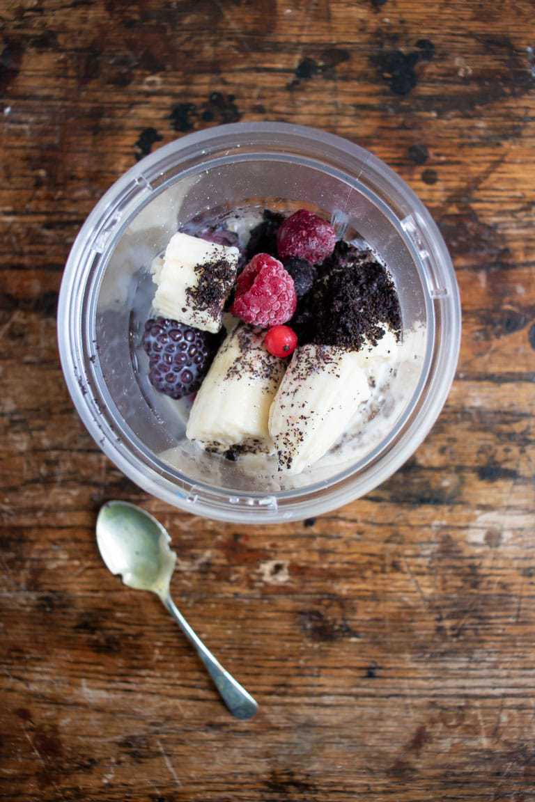 Ingredients for acai smoothie bowl in a blender - banana, plant milk, acai powder, frozen berries, oats, vanilla, maple syrup.