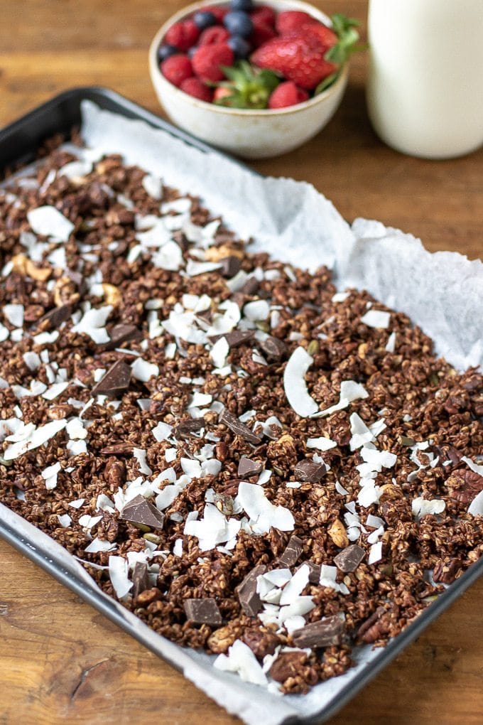 A tray of chocolate coconut granola next to fresh berries.