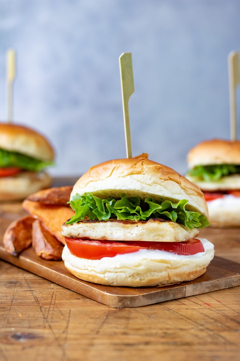 Side view of a cajun halloumi burger, with lettuce, tomato and brioche bun. With a skewer through it.