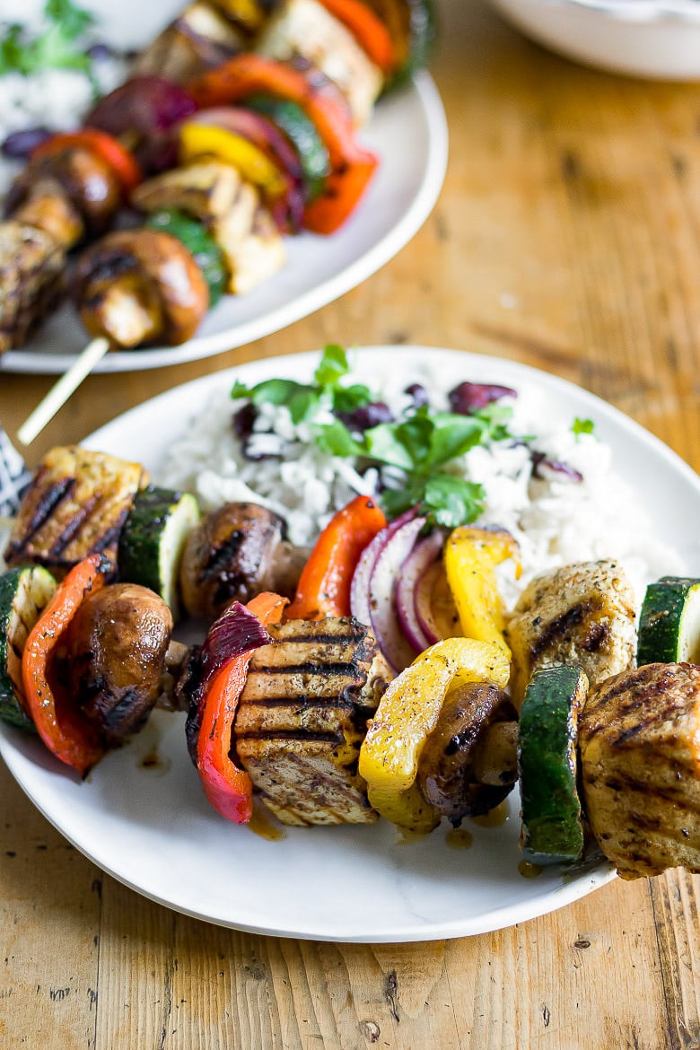 Close up of grilled jerk tofu on skewers with vegetables, shown on a plate with Jamaican rice and peas