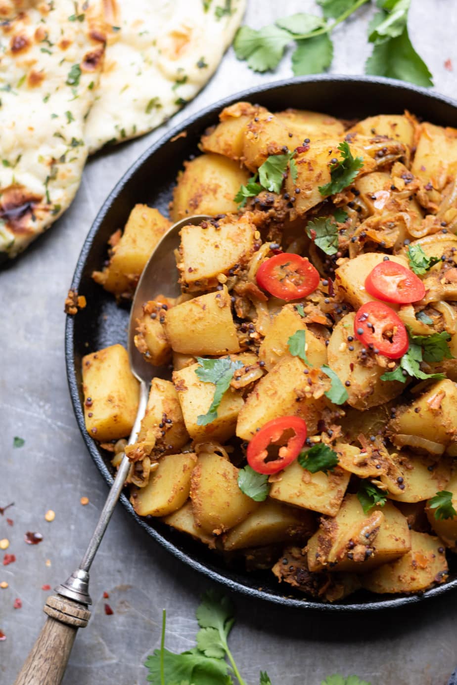 A dish of Bombay Potatoes, with naan and sprinkled with coriander and red chillis.