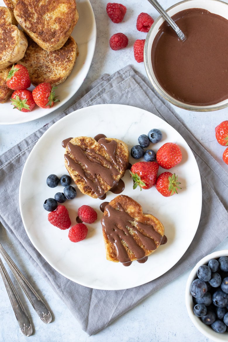A plate with two heart-shaped cinnamon french toast with chocolate sauce and berries
