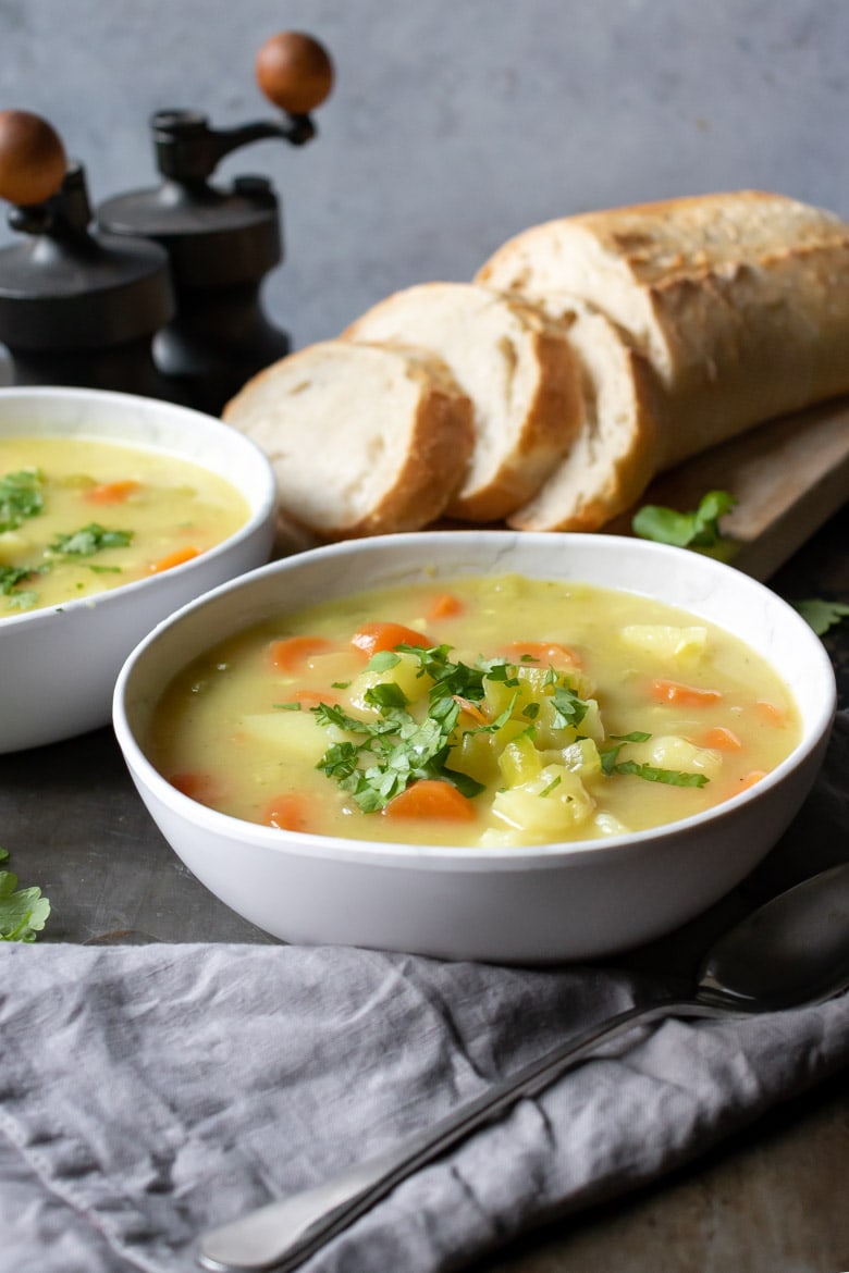Bowl of vegan stew full of vegetables and potato, with bread in the background.