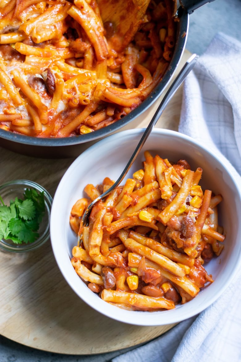 A bowl of vegan chili mac next to a pot of it and some parsley.