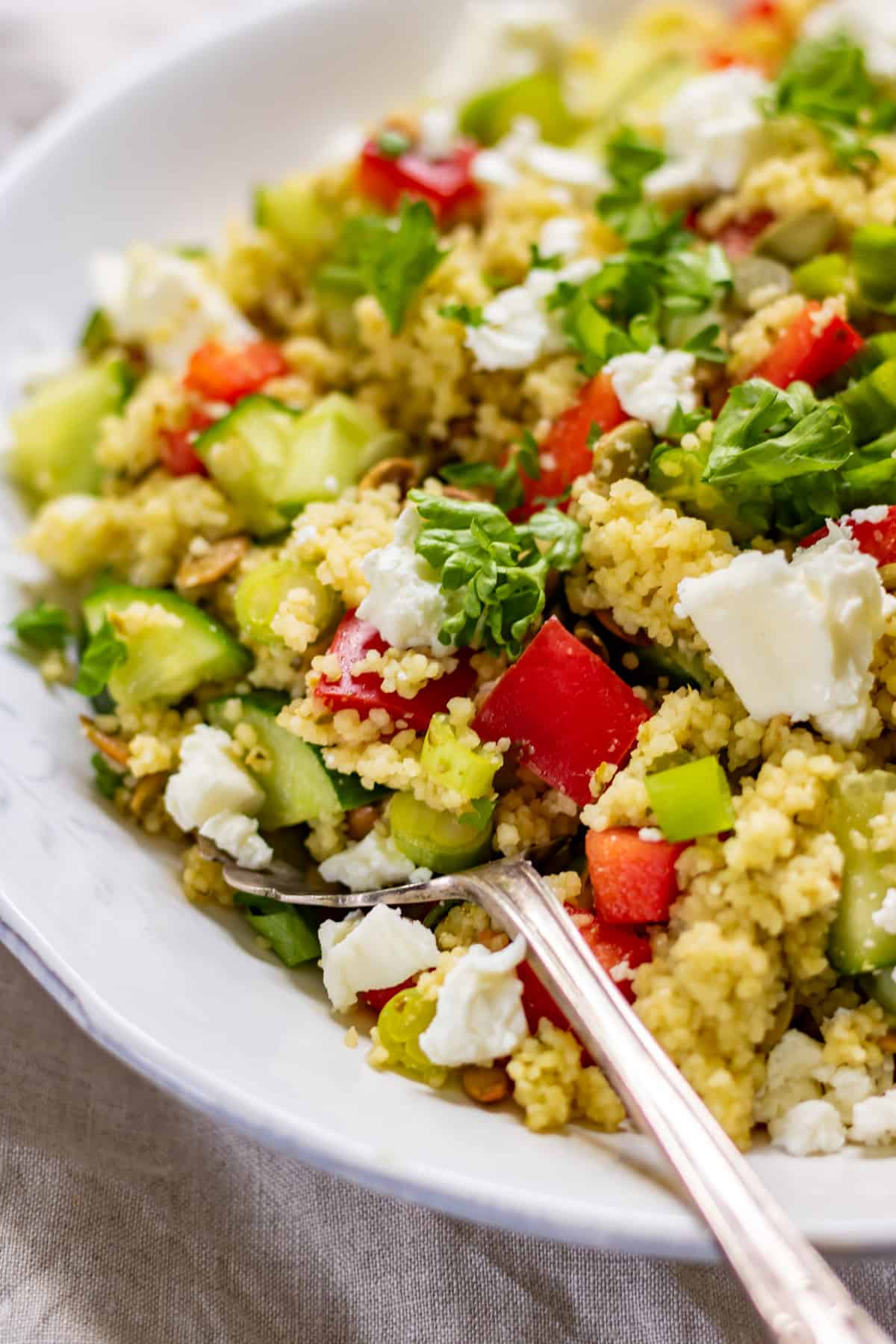 Close up of a spoon in a serving dish of couscous salad.