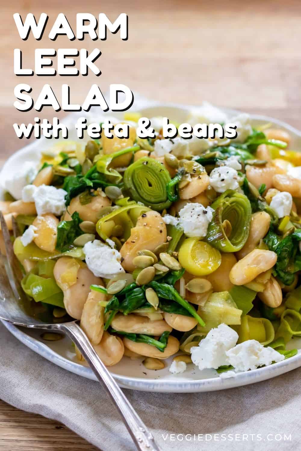 Plate of salad on a table, with text: warm leek salad with feta and beans.