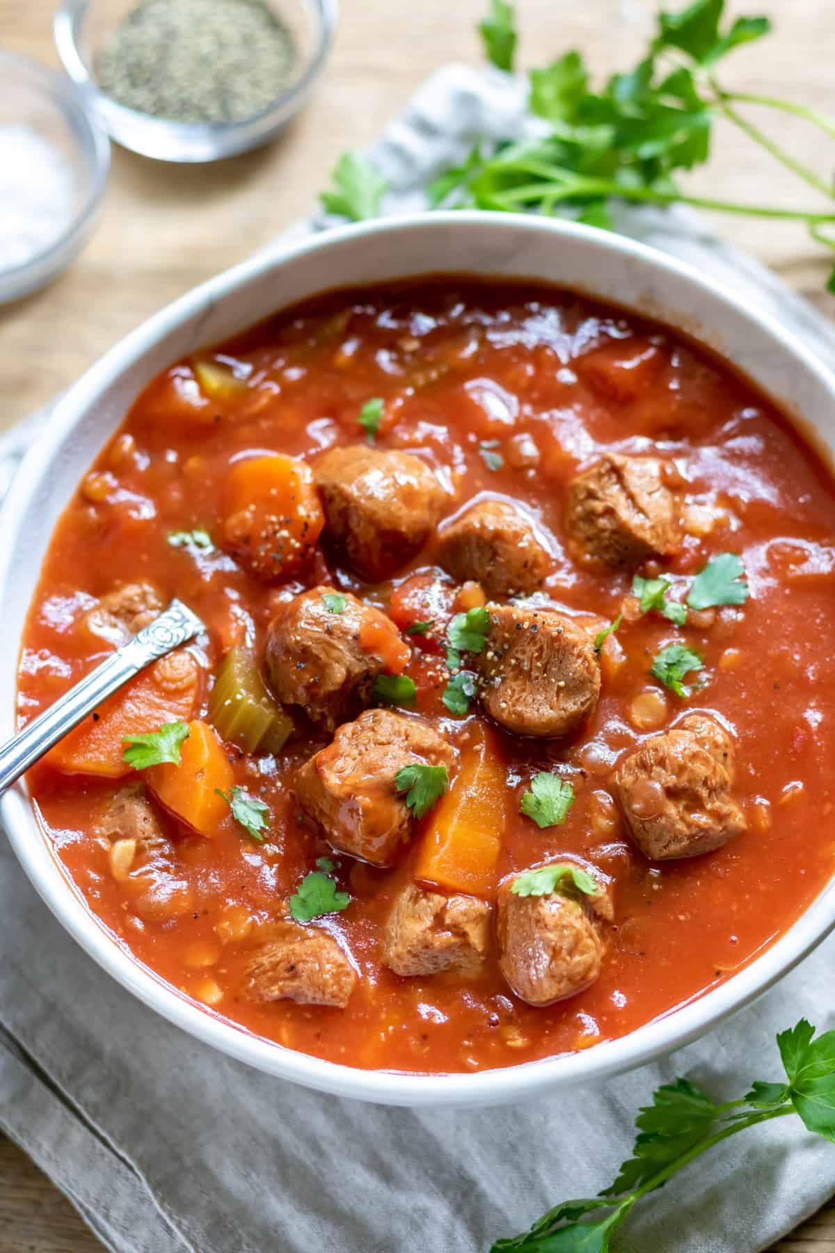Table with a dish of vegan stew, next to a napkin and bowl of salt and pepper.