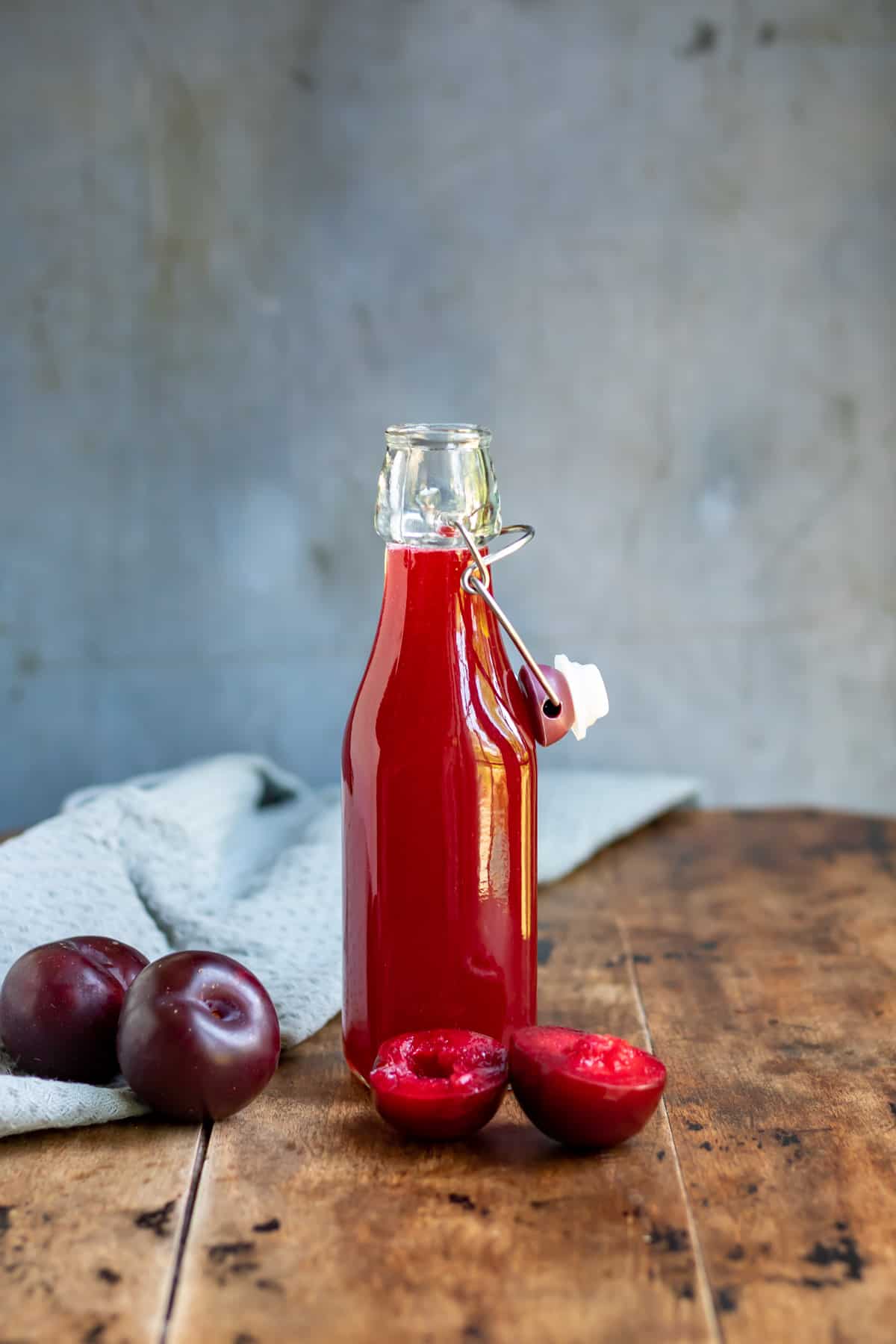 Wooden table with a bottle of plum syrup and some plums.