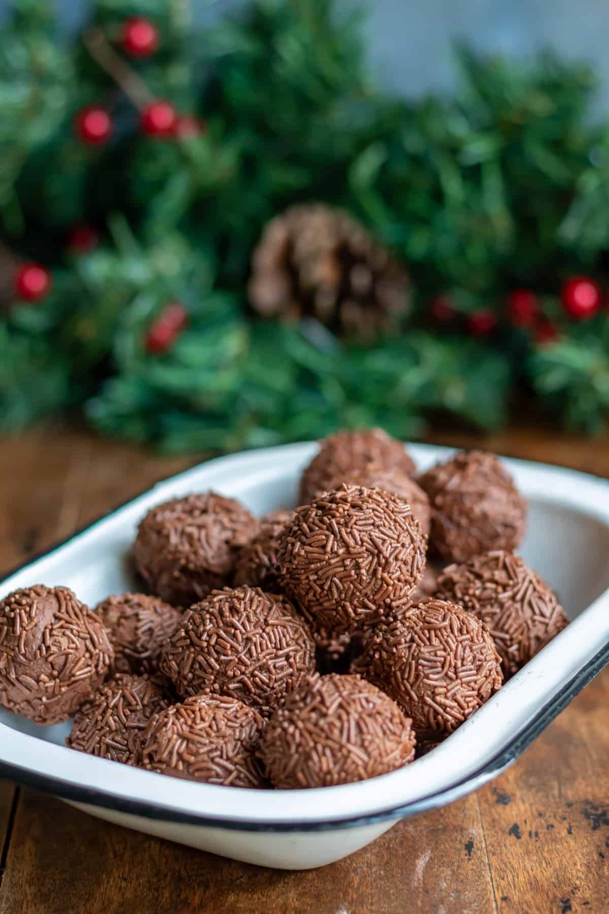 Dish of rumkugeln rum balls on a wooden table in front of a Christmas pine garland.