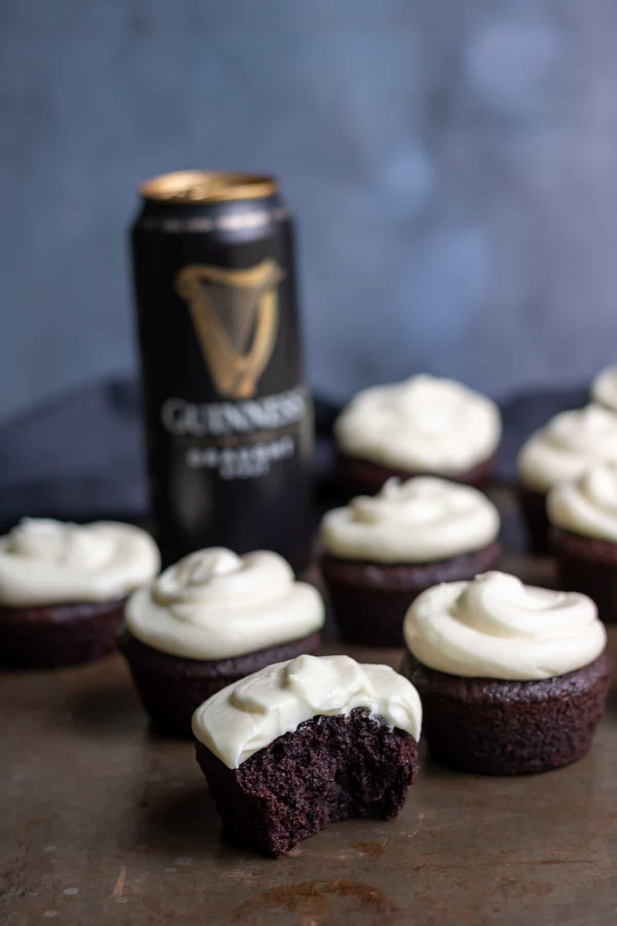 Side view of Guinness chocolate cupcakes topped with cream cheese frosting, with one in front with a bite out.