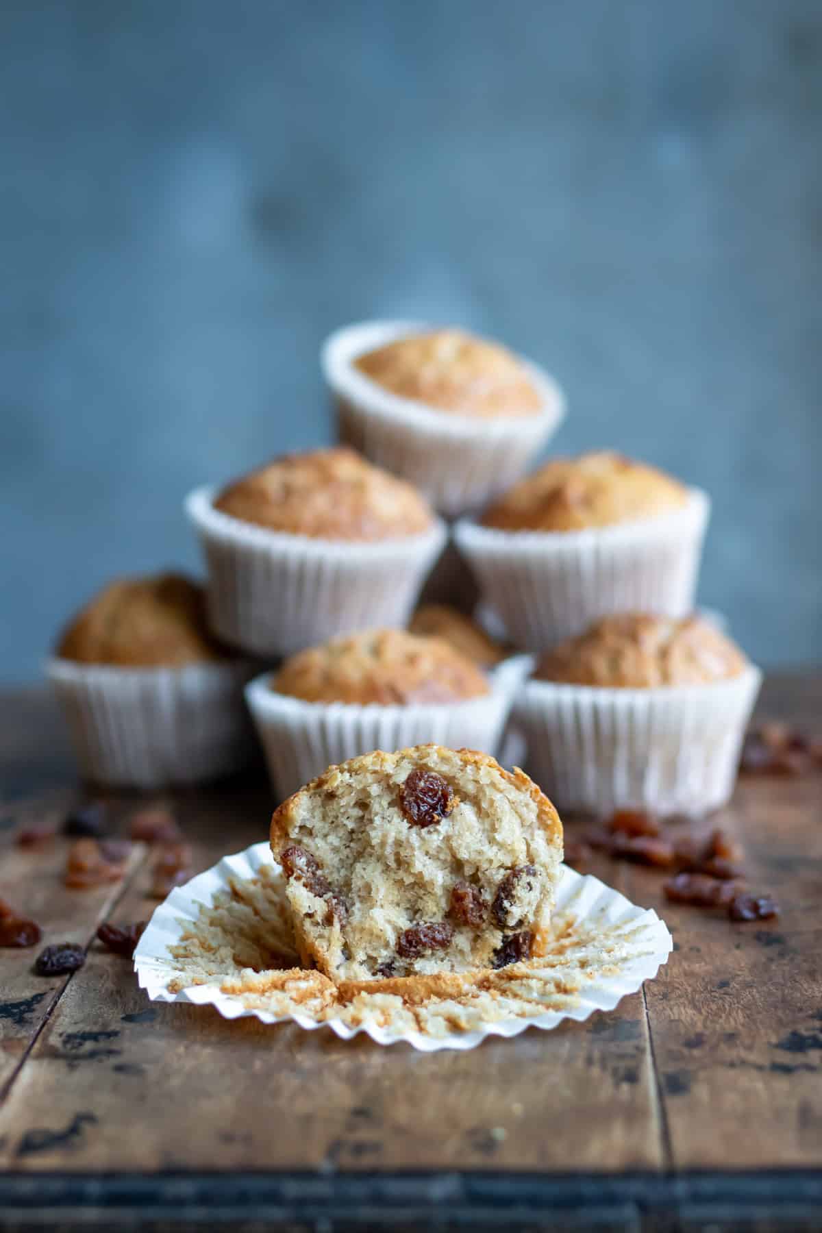 Side view of a table with a raisin muffin with a bite out in front of a pile of muffins.