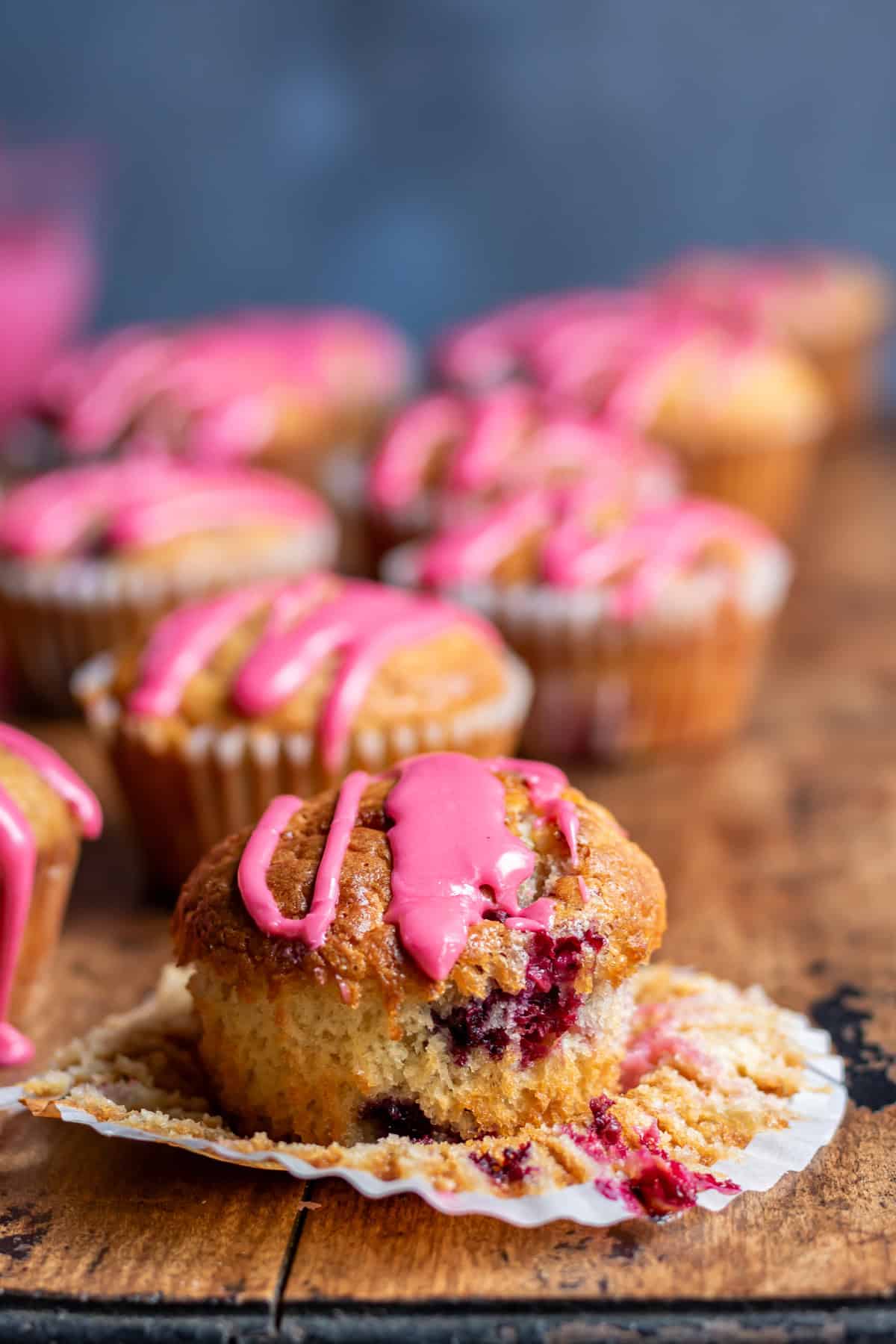 A frozen berry muffin with the paper case peeled down, in front of more muffins.