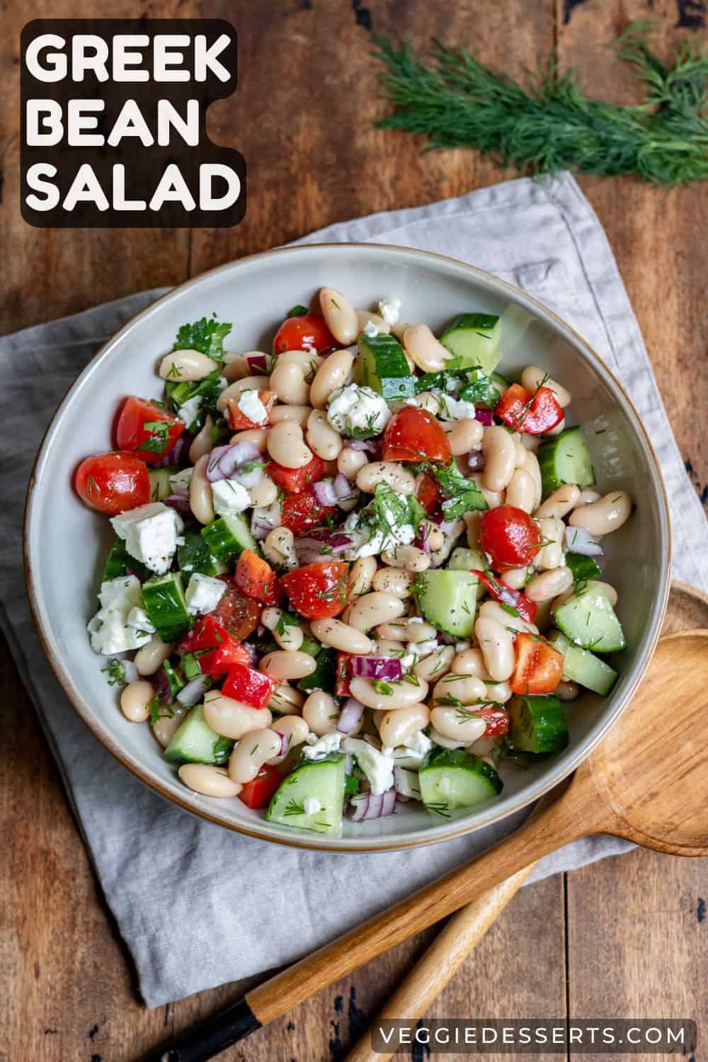 Bowl of salad on a table, with text: Greek Bean Salad.