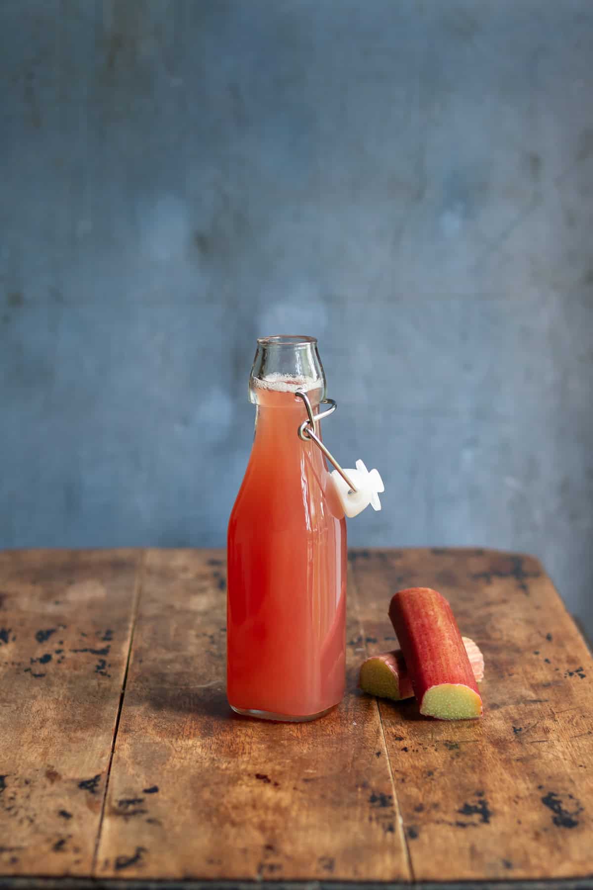 A wooden table with a glass bottle of rhubarb simple syrup.