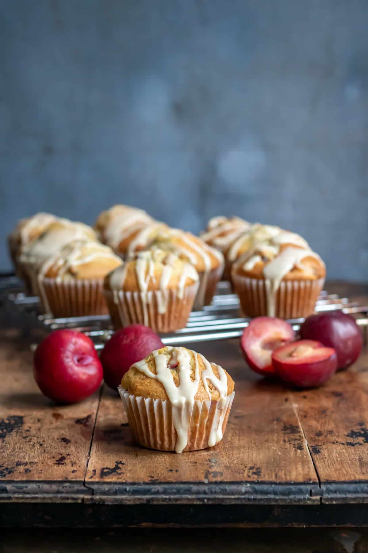 Side view of plum muffins on a wooden table next to fresh plums.