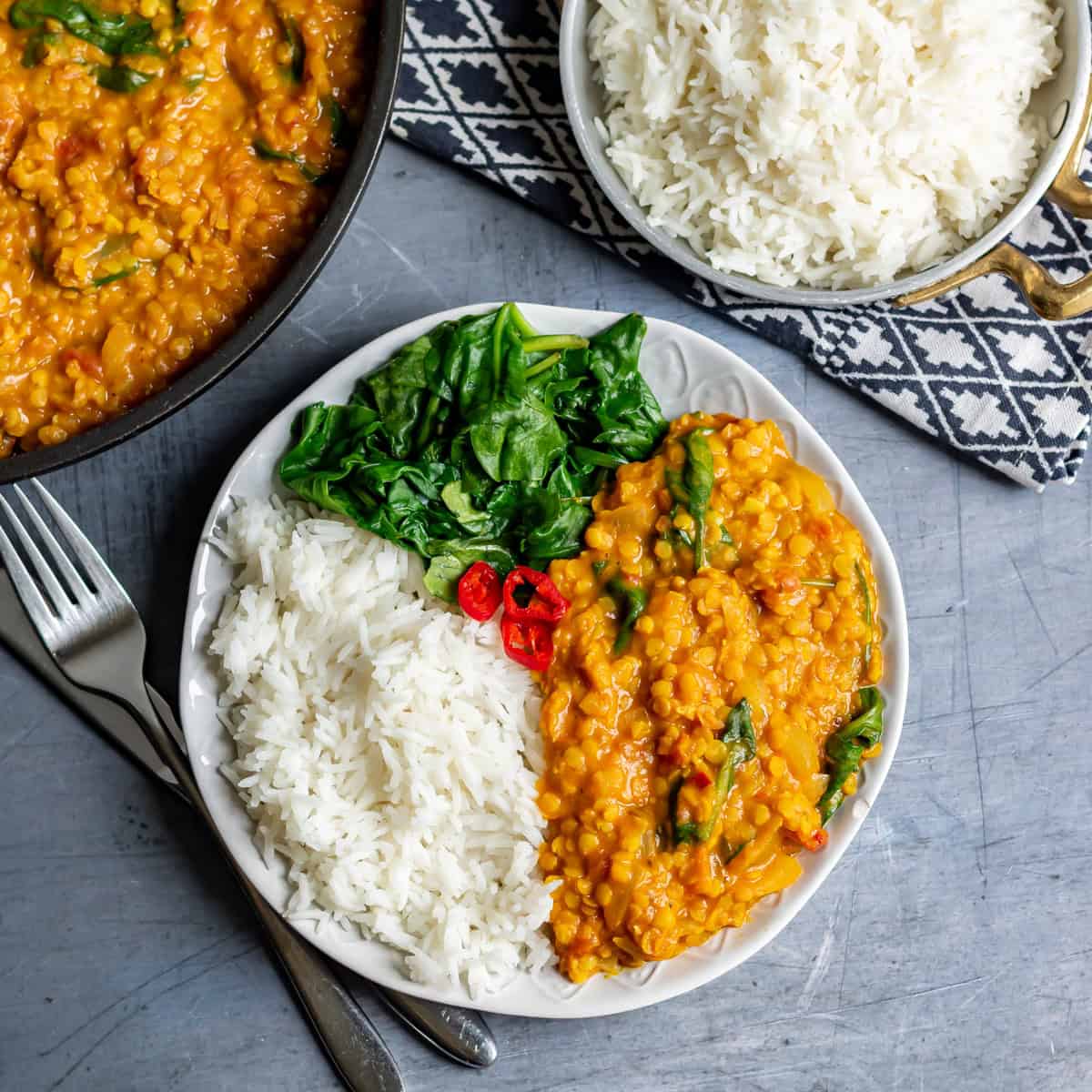 Close up of a plate of red lentil dahl with rice and spinach.