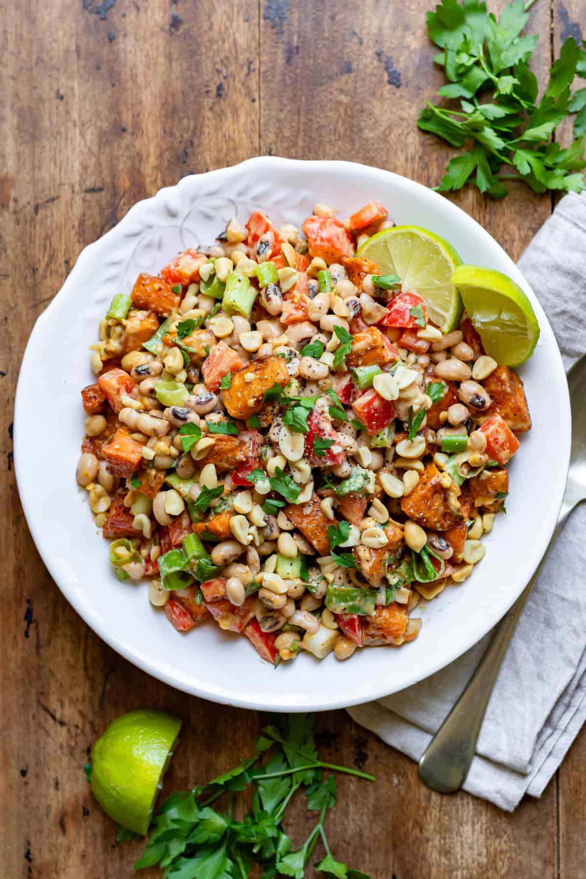 Looking down at a wooden table with a serving dish of sweet potato black eye peas salad with peanut dressing.