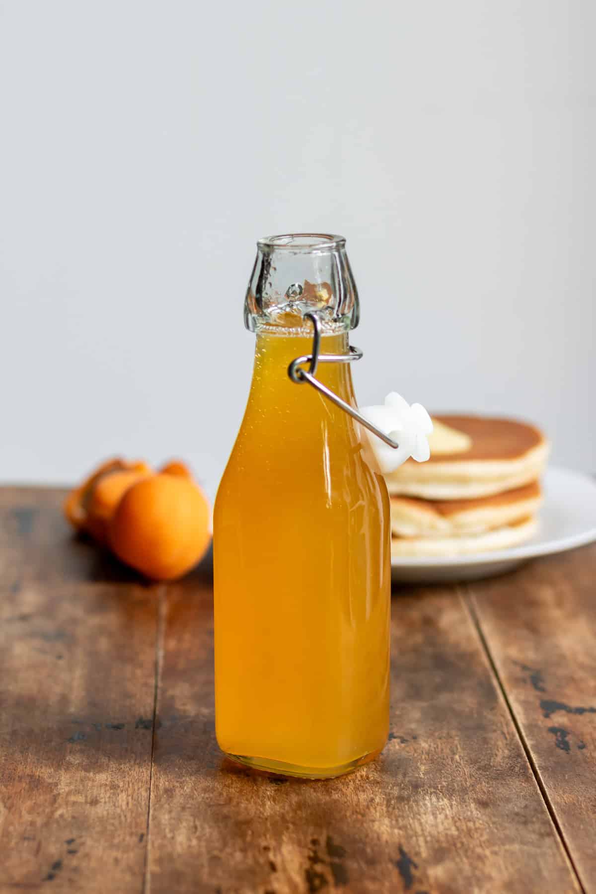 Bottle of apricot syrup on a table in front of pancakes.