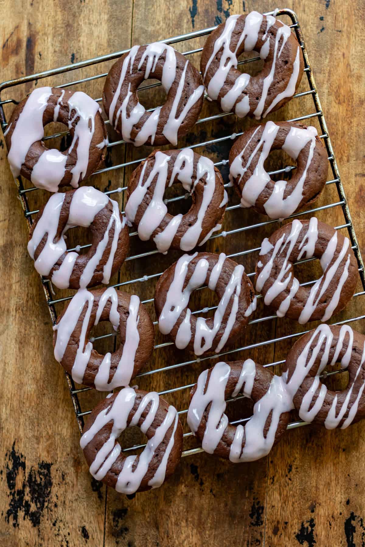 Looking down at a wire rack of beet chocolate donuts on a wooden table.